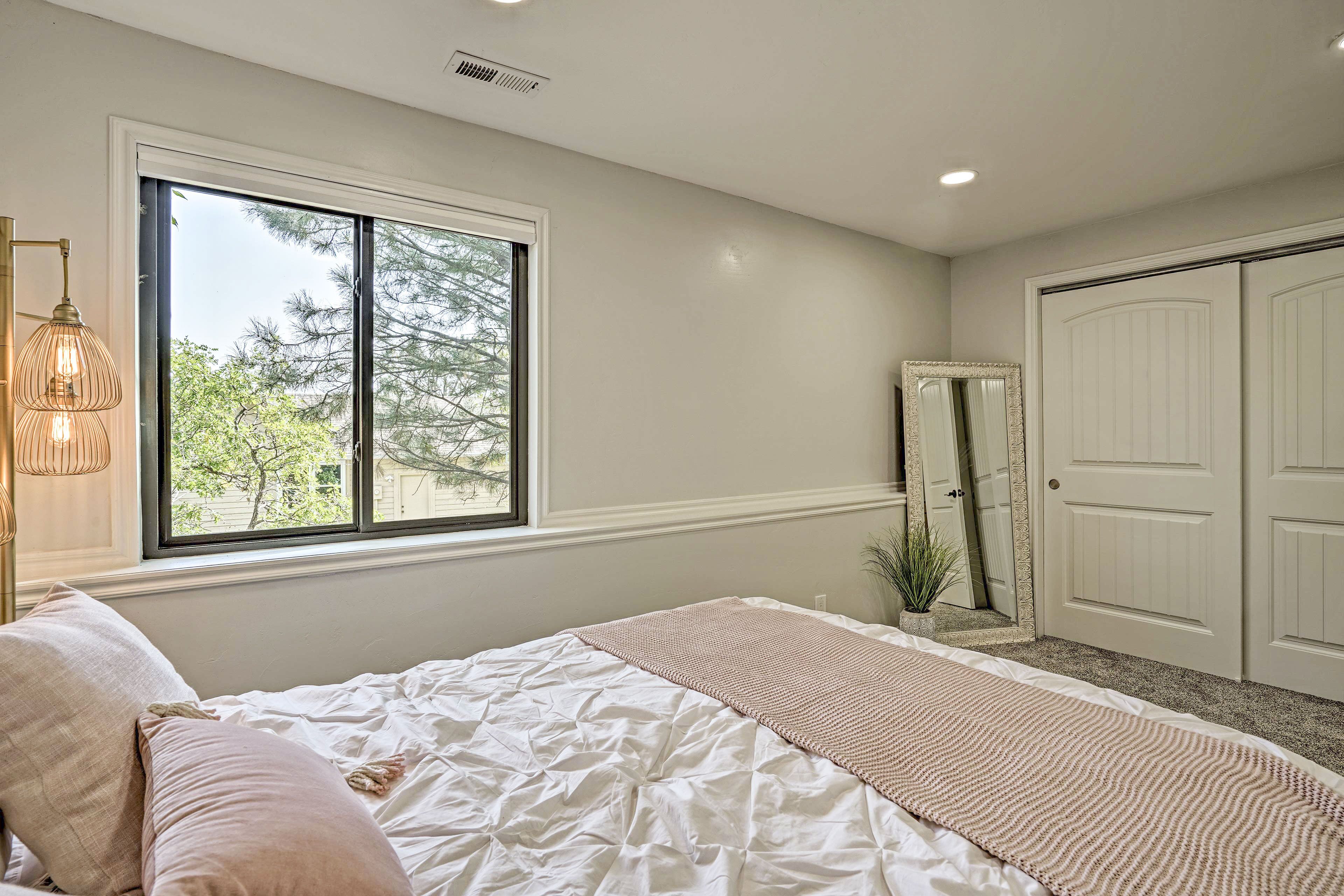 A bedroom with a large bed, a window with a view of trees, a door, and a mirror.