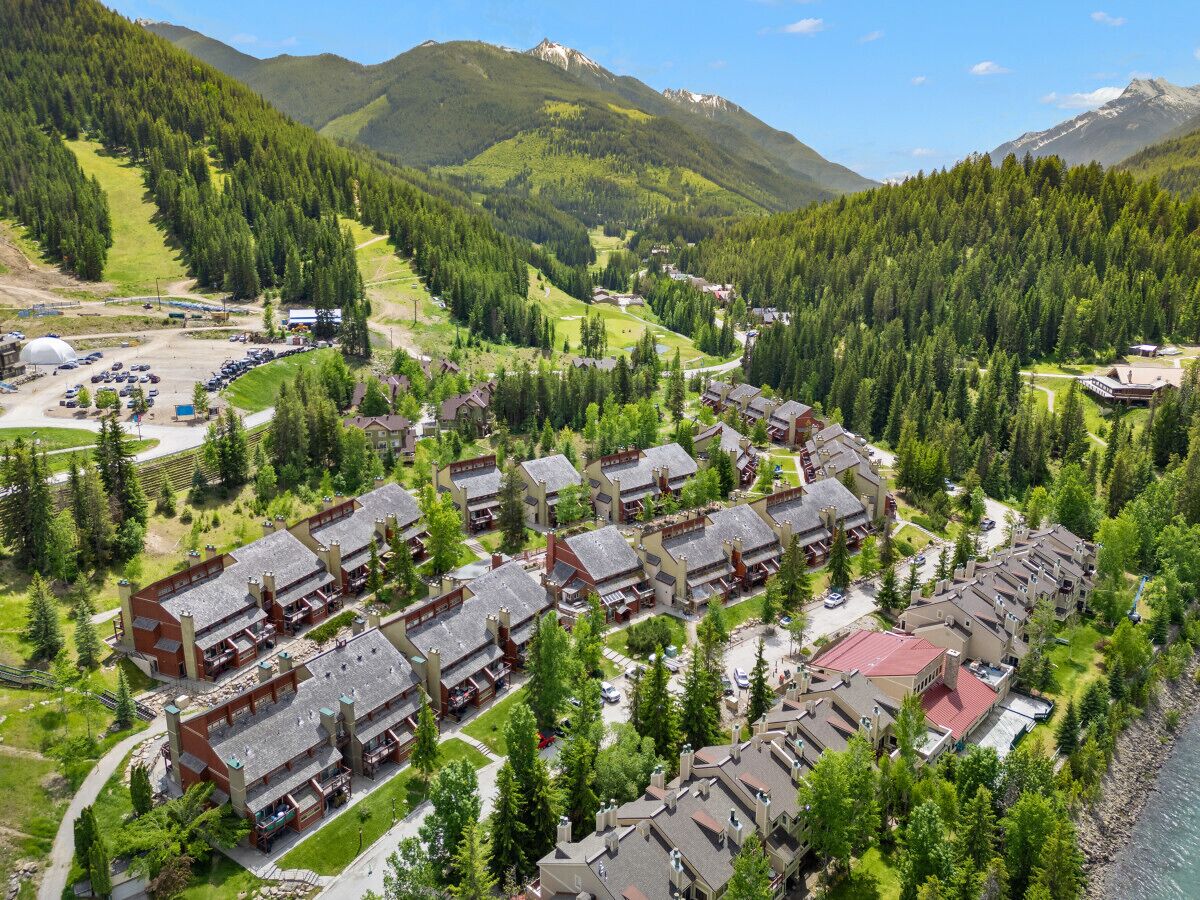 A resort with multiple chalet-style buildings arranged in a row, surrounded by dense forest and mountains.