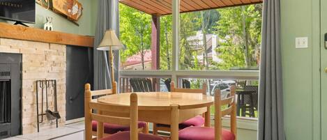 A dining area with a wooden table and chairs, a fireplace, and a large window with a view of greenery outside.