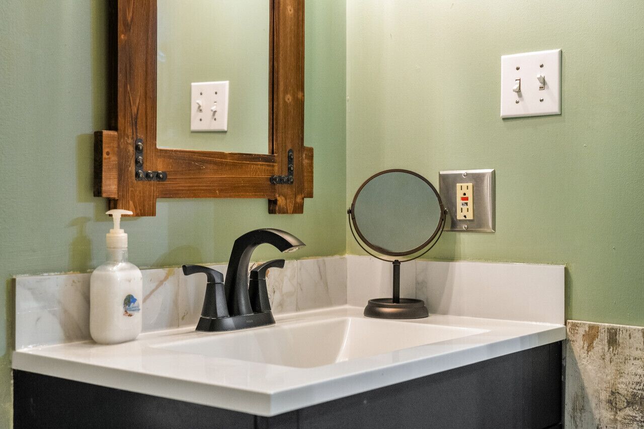 A bathroom with a white sink, a mirror, a soap dispenser, and a wooden-framed mirror above the sink.