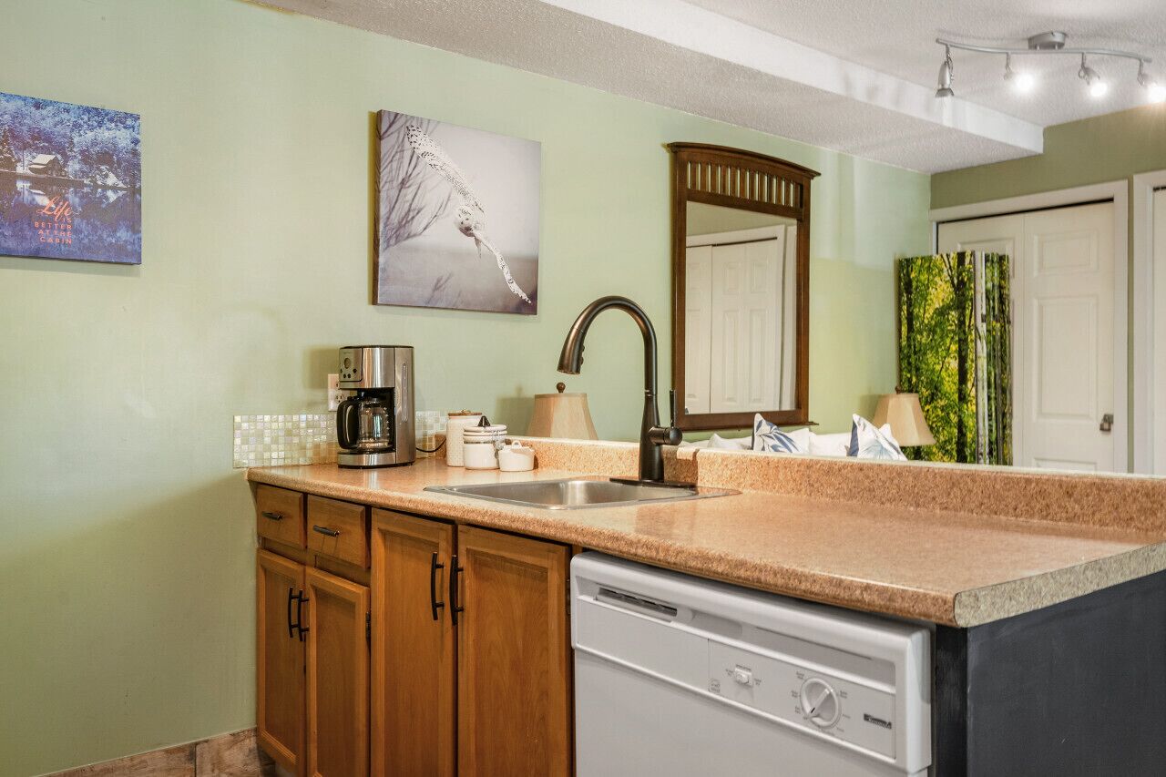 A kitchen with a dishwasher, a coffee maker, and a sink. There are wooden cabinets and a countertop.