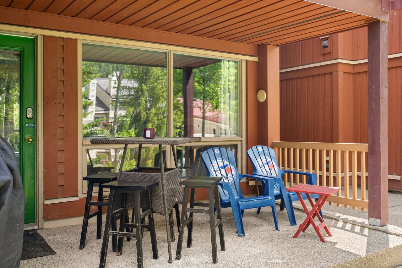 An outdoor seating area with tables and chairs, a green door, and a view of trees and buildings.