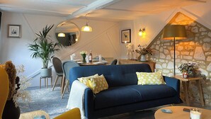 A cozy living room with a blue sofa, yellow armchairs, a dining table, and a stone wall.