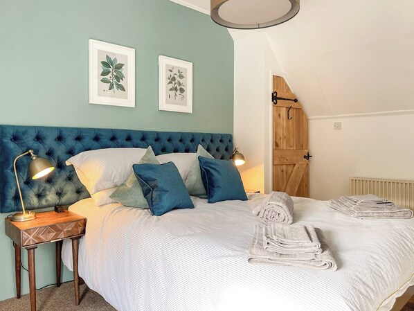A bedroom with a tufted headboard, a bedside table with a lamp, a bed with white bedding and blue pillows, and two framed botanical prints on the wall. - 2 bedroom accommodation in Calbourne (Calbourne)