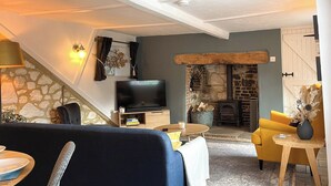 A cozy living room with a blue sofa, a yellow armchair, a TV, a fireplace, and a stone wall.