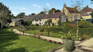 A courtyard with a stone building, a grassy lawn, and a potted plant.