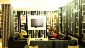Una sala moderna con un televisor de pantalla plana montado en la pared, un conjunto de sofás y un diseño de papel tapiz estampado.