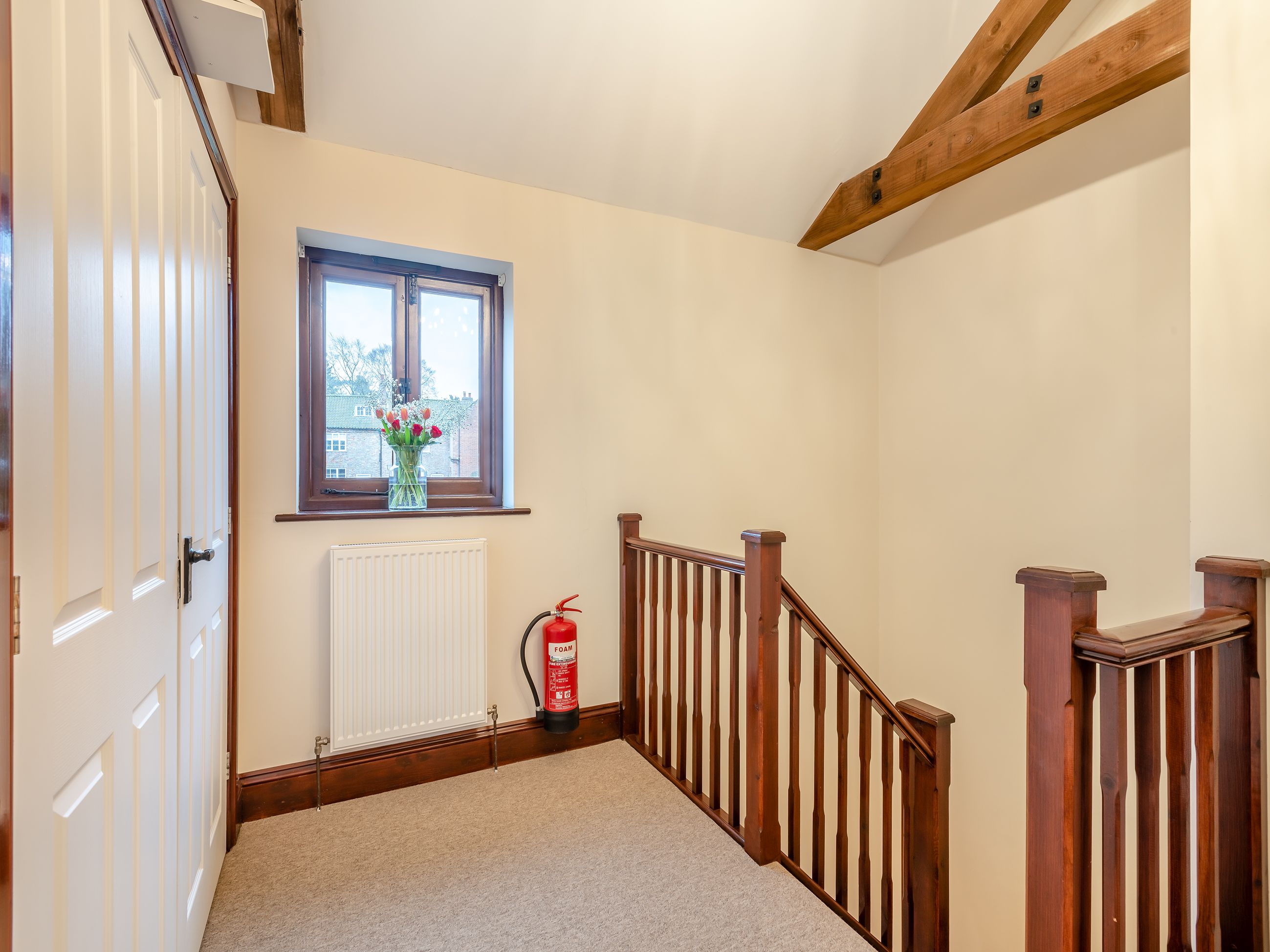 A hallway with a wooden staircase, a white radiator, and a window with a vase of flowers.