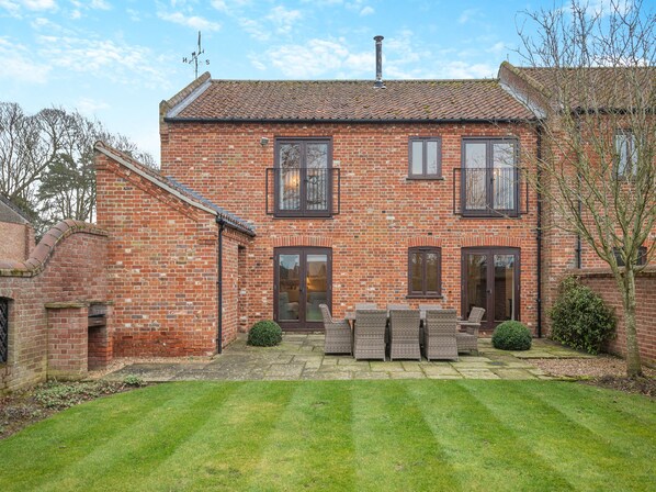 A two-story brick house with a patio area featuring wicker furniture and a lawn.