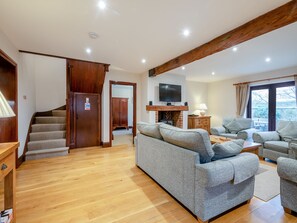 A spacious living area with a wooden staircase, a fireplace, a television, and multiple seating options.