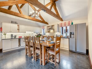 A modern kitchen with wooden beams, a dining table set for four, and a refrigerator. - WOODPECKER BARN - CWL (Sculthorpe, Fakenham)