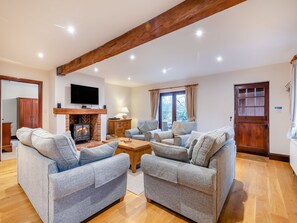 A cozy living room with a fireplace, two grey sofas, a wooden coffee table, and a television mounted above the fireplace.