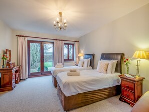 A bedroom with two beds, a chandelier, a nightstand, and a view of the outdoors.