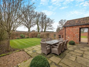 A patio with a glass-top table and wicker chairs, surrounded by a brick wall and a grassy lawn. - WOODPECKER BARN - CWL (Sculthorpe, Fakenham)