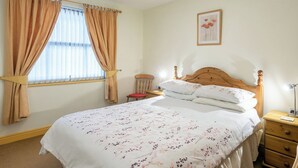 Un dormitorio con una cama de madera, una mesita de noche, una silla y una ventana con cortinas.