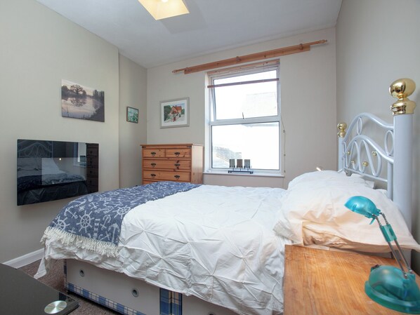 A bedroom with a bed, a dresser, a TV mounted on the wall, and a window with a view of the outside. - Northumberland apartment (Teignmouth)