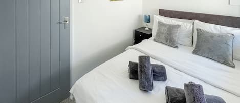 Una habitación de hotel con cama, almohadas, mesita de noche, lámpara y puerta.