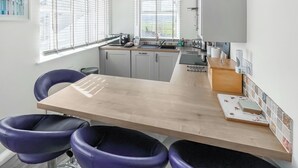 A modern kitchen with a wooden countertop, two purple chairs, a sink, and a window with blinds. - 2 bedroom accommodation in Levens, near Kendal (Levens, near Kendal)