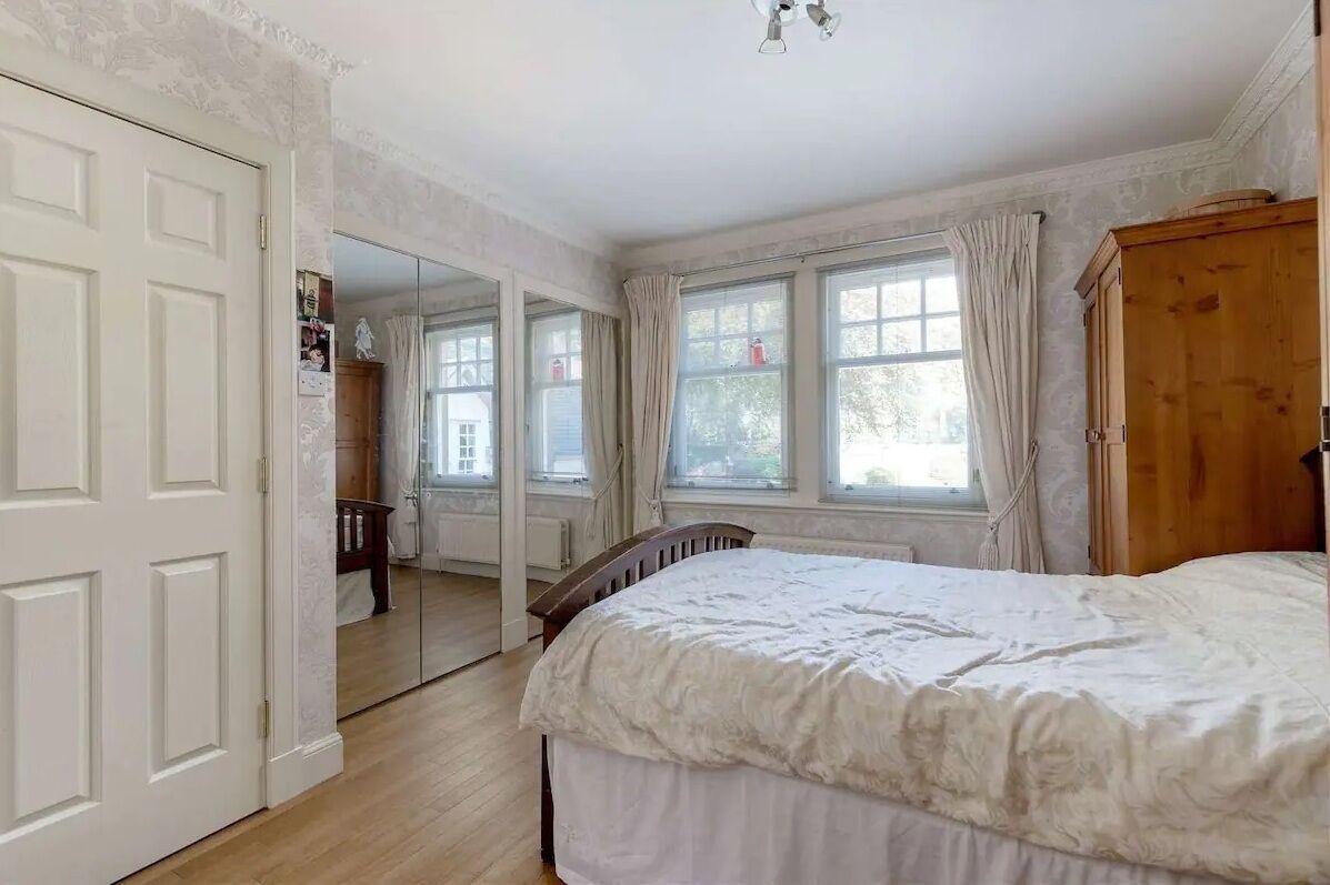 A bedroom with a large bed, a wooden wardrobe, and a window with curtains.