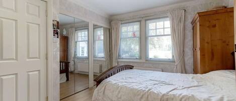 A bedroom with a large bed, a wooden wardrobe, and a window with curtains.