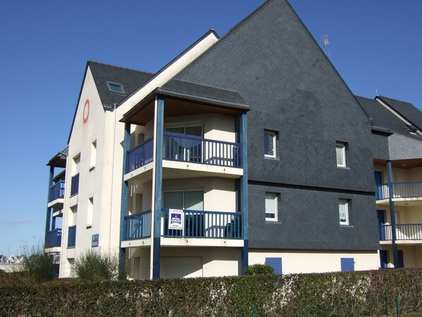 A multi-story building with balconies, a visible sign, and a clear sky.