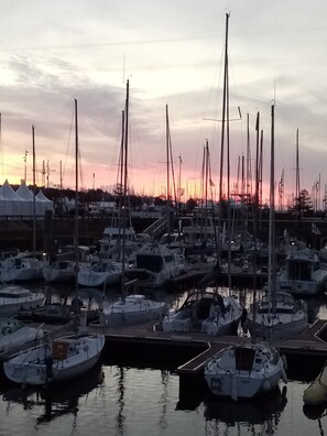 Un puerto deportivo con varias embarcaciones amarradas, superficie de agua tranquila y un atardecer de fondo.
