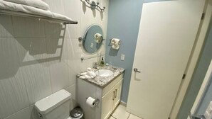 A bathroom with a toilet, sink, and mirror. There are towels on the wall and a door to the right. - Condos Tiara (Mazatlán)