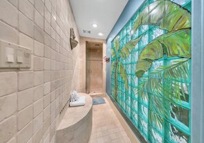 Un bagno con parete piastrellata, zona doccia e un divisorio in vetro con motivo a foglia.