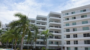 A modern hotel with multiple floors, a swimming pool, and palm trees. - Depas Veleros (Mazatlán)