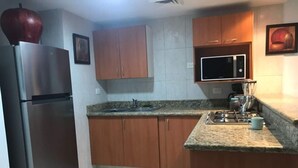 A kitchen with wooden cabinets, a stainless steel refrigerator, a microwave, and a gas stove. - Depas Veleros (Mazatlán)