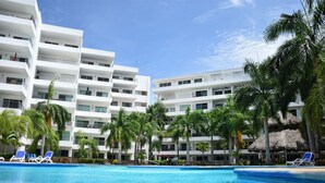 A hotel with a swimming pool, palm trees, and a thatched-roof structure. - Depas Veleros (Mazatlán)