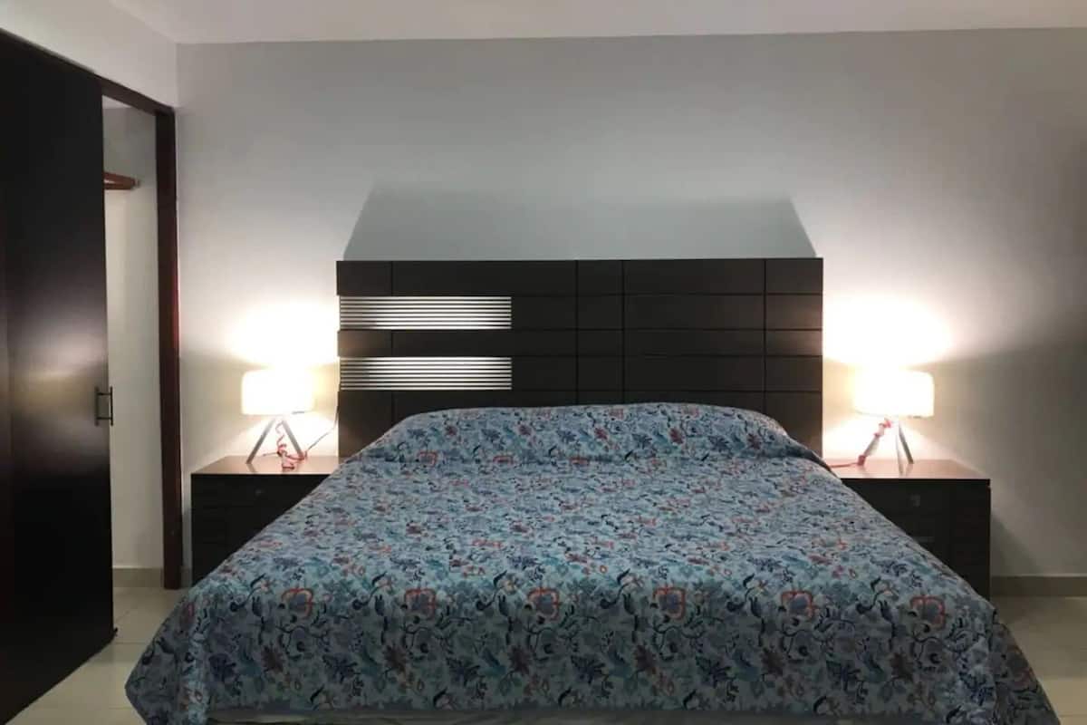 Ein Schlafzimmer mit einem Bett, zwei Nachttischen und einem Kopfteil mit integrierter Beleuchtung.