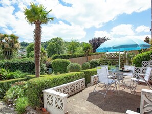 A patio area with a table and chairs, surrounded by well-maintained hedges and a wooden fence. - 2 bedroom accommodation in Brixham (Brixham)