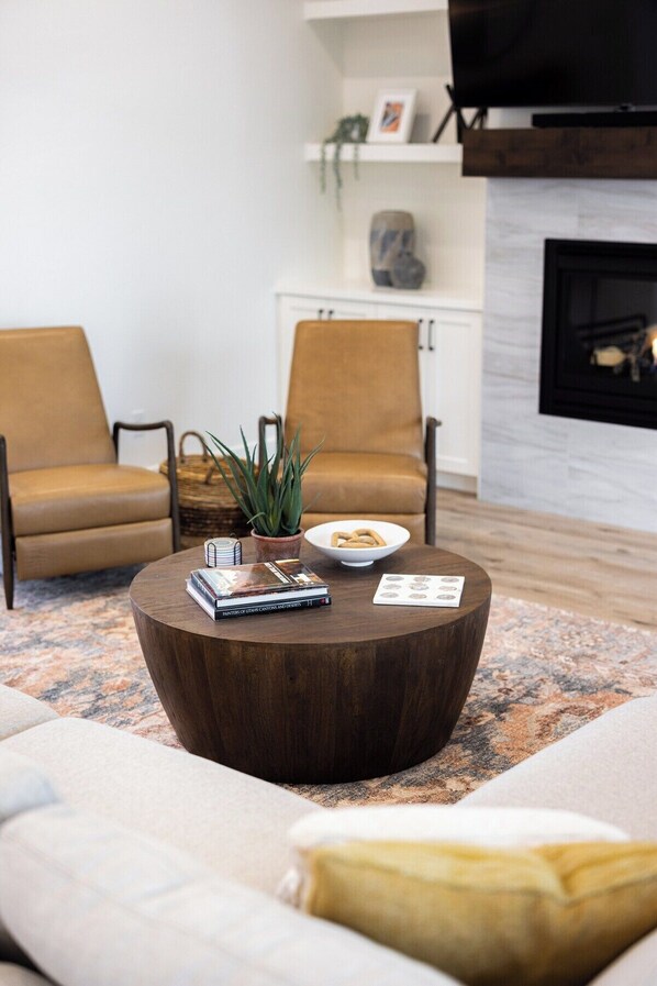 A modern living room with a round wooden coffee table, two armchairs, a sofa, and a fireplace.