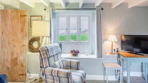 A cozy room with a plaid armchair, a television, and a window with a view of a green field. - 3 bedroom accommodation in Kettleness, near Whitby (Kettleness, near Whitby)