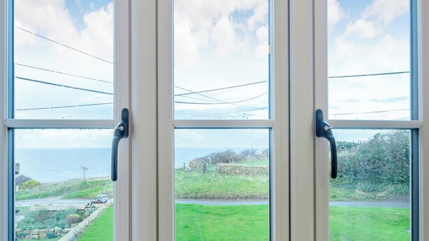 A view through a window with a stone wall and grassy field, with a road and a body of water in the distance. - 3 bedroom accommodation in Kettleness, near Whitby (Kettleness, near Whitby)