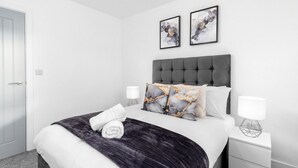 A neatly arranged bedroom with a large bed, two bedside tables, and two framed artworks on the wall. - The Marsons Collection- 2 Bed Apartment- Parking (Birmingham)