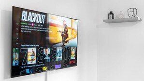 A TV mounted on a wall displaying a movie poster for "Blackout" and a shelf with a few items above it. - The Marsons Collection- 2 Bed Apartment- Parking (Birmingham)