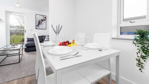 A modern dining area with a white table set for two, a glass coffee table, and a view of the outdoors. - The Marsons Collection- 2 Bed Apartment- Parking (Birmingham)