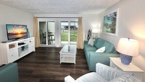 A living room with a TV, a sofa, a coffee table, and a lamp. - Beach Chairs For 4 • 1st Floor • Sleeps 6 (Panama City Beach)