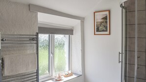 Un baño con ventana, perchero, un cuadro enmarcado y ducha.
