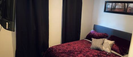 A bedroom with a bed, black curtains, a mounted TV, and a framed picture on the wall.