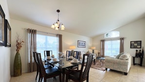 A dining area with a glass table, dark chairs, and a chandelier. There is a sofa and a side table with lamps in the living area. - Serenity By Your Private Pool! Excellent Reviews! Resort Living! 4450 (Kissimmee)