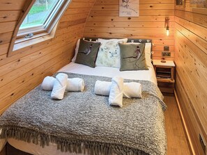 A cozy wooden cabin bedroom with a bed, pillows, a blanket, and a nightstand with a lamp.