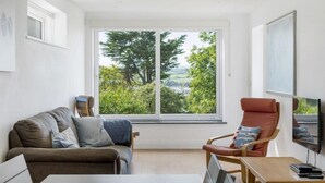 A modern living room with a large window, a sofa, a chair, and a flat-screen TV. - Spacious Apartment in Rock, Private Parking (Rock)
