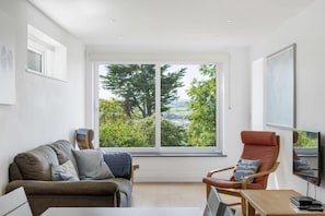 Un salon moderne doté d’une grande fenêtre, d’un canapé, d’un fauteuil et d’un téléviseur à écran plat.