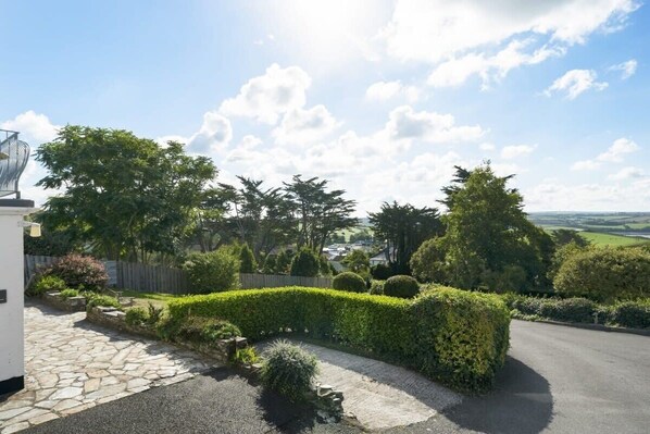 A residential driveway with a stone pathway leading to a white building, surrounded by well-maintained hedges and trees.