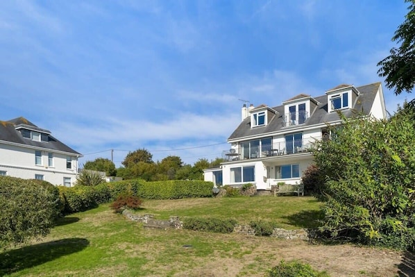 Une maison à deux étages avec une grande pelouse devant, un balcon à l’étage supérieur et une antenne parabolique.