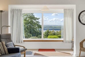 A room with a large window offering a scenic view of greenery and hills.