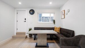 A modern living room with a dining table, sofa, and a staircase leading to an upper level.